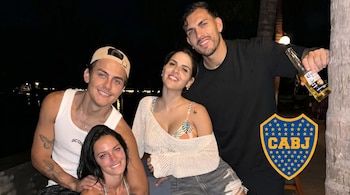 Cuatro personas sonríen a cámara de noche. Leandro Paredes sostiene una cerveza, Paulo Dybala lleva gorra. Escudo de Boca Juniors en esquina inferior derecha.