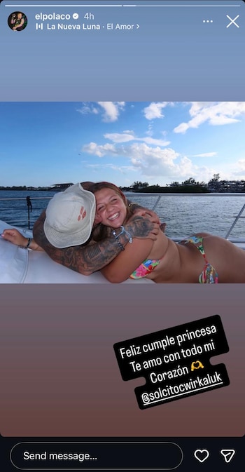 Un hombre tatuado con gorra abraza a una mujer joven sonriente en bikini, a bordo de una embarcación en el agua bajo un cielo azul con nubes