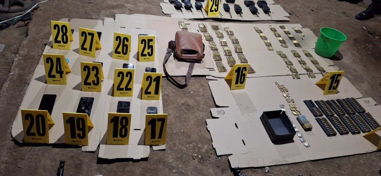 Evidencia de un importante operativo policial muestra municiones, radios bidireccionales, teléfonos inteligentes y una bolsa de cuero dispuestas con marcadores numéricos. (PNCdeGuatemala)