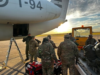 Cola y fuselaje de un avión de carga, personal militar con uniformes de camuflaje, vehículo de apoyo terrestre, generador eléctrico rojo, escalera