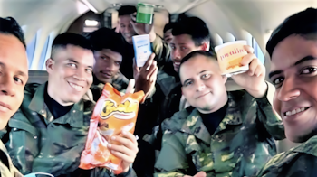 Hombres con uniformes de camuflaje posan dentro de una aeronave mientras sostienen una bolsa de frituras y envases de alimentos