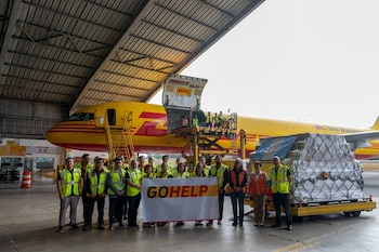 Un grupo de personas con chalecos de seguridad sostiene un cartel de GoHelp frente a un avión amarillo y palés con carga