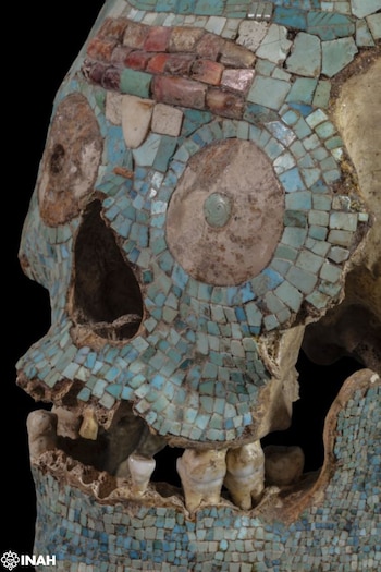 Cráneo con incrustaciones de mosaico de turquesa, concha y fragmentos de colores. Se aprecian las cuencas de los ojos, la cavidad nasal y los dientes