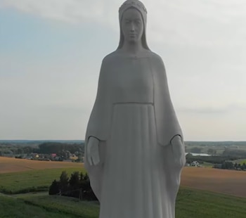 Estatua de Buda de piedra blanca con una corona en la cabeza, túnica, y manos extendidas; campos verdes, árboles, cielo despejado