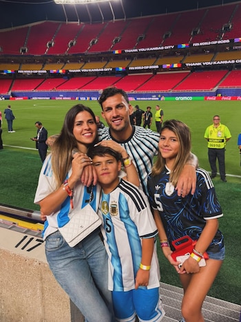 Un hombre, una mujer, un niño y una niña posan sonriendo en un estadio de fútbol con gradas rojas, césped verde y carteles del Mundial FIFA 2026