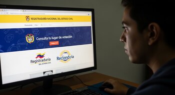 Un hombre joven de perfil derecho mira una pantalla de computadora que muestra un portal web falso de la Registraduría para consultar lugar de votación.