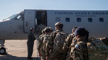Un grupo de militares con uniformes de camuflaje y mochilas embarca en un avión gris de la Fuerza Aérea Argentina que dice "T-9"