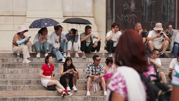 Turistas se refugian con paraguas y gorros en las escaleras de la Opéra de París, en plena ola de calor. (EFE/ Edgar Sapiña)
