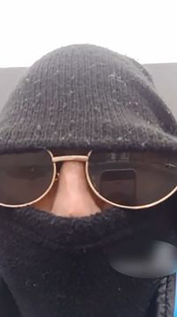 Primer plano de una persona que lleva un pasamontañas negro, un gorro de lana oscuro y gafas de sol con montura dorada y cristales oscuros