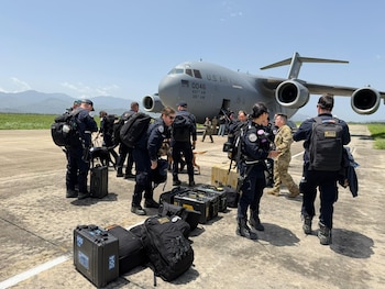 Un avión militar de transporte C-17 Globemaster III en una pista. Varias personas uniformadas, algunos perros, maletas y cajas se observan en la escena