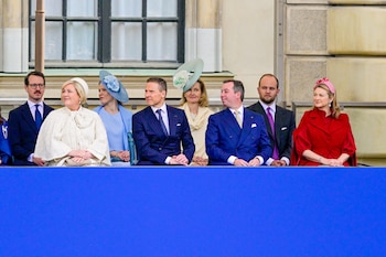 Siete personas de mediana edad y mayores sentadas en primera fila, con cuatro mujeres y tres hombres vistiendo atuendos formales, incluyendo sombreros y trajes