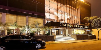 Vista nocturna exterior del Crowne Plaza Lima, un edificio moderno con fachada de cristal y entrada iluminada, y un coche negro estacionado