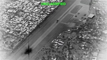 Imagen aérea monocromática de la isla de Kharg con un área urbana densa, una pista y una explosión oscura; texto 'UNCLASSIFIED' visible en verde