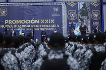 Integrantes de la guardia penitenciaria formados de espaldas frente a un escenario con autoridades y la bandera de Guatemala