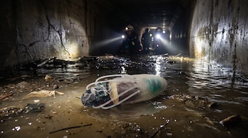 Una cucaracha cíborg con circuito electrónico y tubos en agua turbia dentro de un túnel con escombros. Rescatistas desenfocados con linternas.