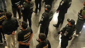Vista superior de varios policías vestidos de negro con chalecos distintivos junto a un grupo de personas detenidas