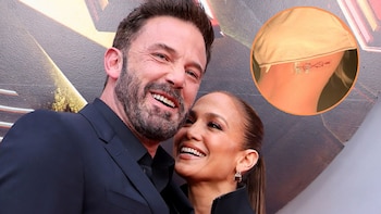 Ben Affleck y Jennifer Lopez sonríen ampliamente. Una imagen circular insertada muestra un tatuaje con un símbolo de infinito y flecha en el cuello de Lopez