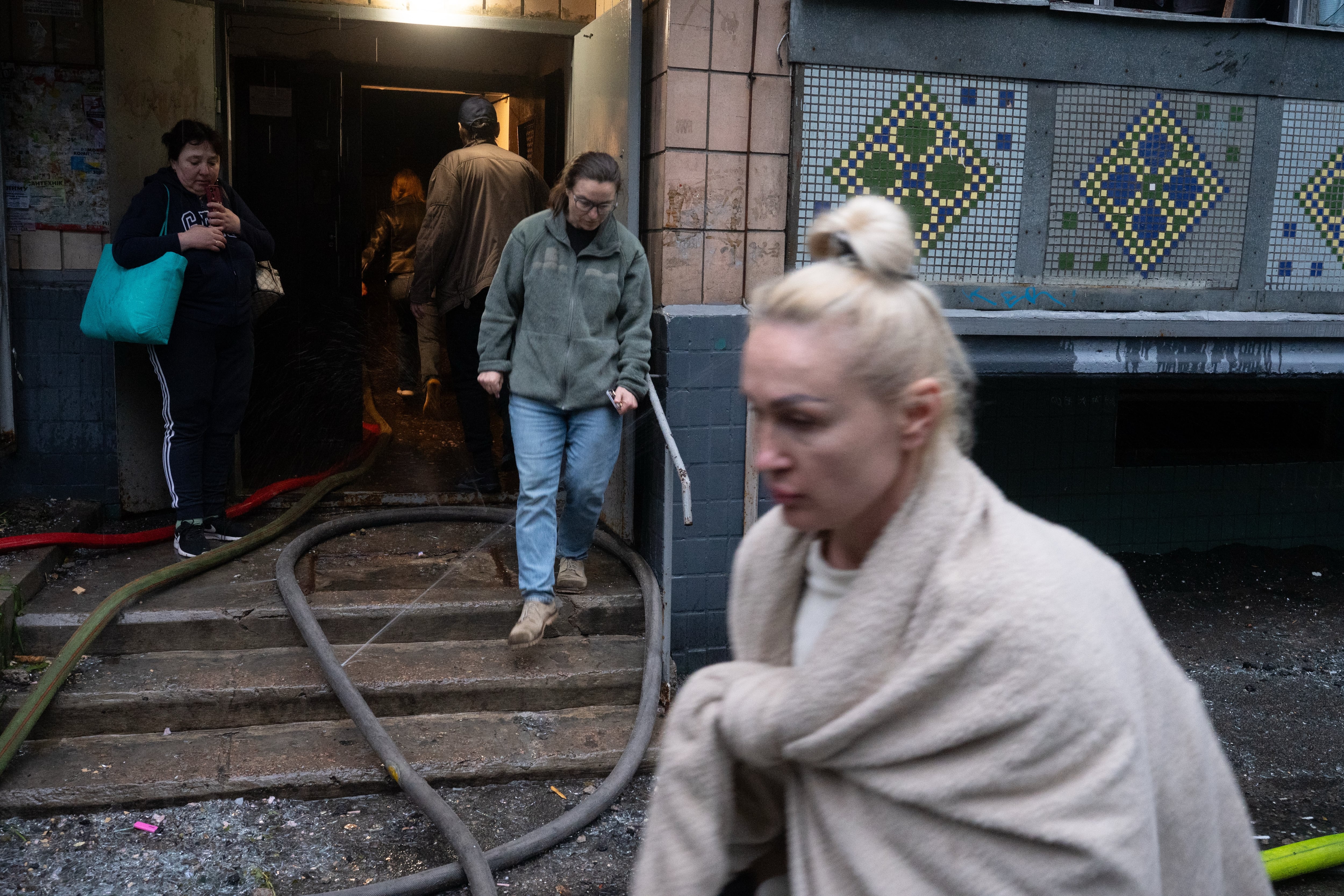 Vecinos se congregan frente a un edificio residencial dañado en Kiev tras el ataque ruso. Los bombardeos alcanzaron numerosos barrios de la capital y dejaron al menos cinco muertos y 34 heridos. (AP Photo/Danylo Antoniuk)