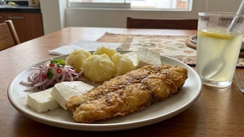 Plato con milanesa frita, papas hervidas, trozos de queso fresco, ensalada de cebolla y un vaso con limonada en una mesa de madera