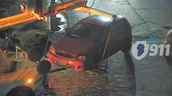 Una grúa engancha y levanta la parte delantera de un automóvil rojo sobre el asfalto durante la noche