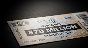 Primer plano de un ticket de lotería beige con el texto 'WINNING $78 MILLION' en el centro, sobre un fondo oscuro con iluminación dramática.