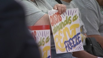 Primer plano de varias personas sosteniendo carteles de protesta que dicen "Queens demands a rent freeze" en letras de colores vibrantes