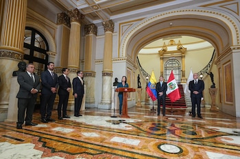 Una mujer habla en un podio ante varios hombres en traje, con banderas de Ecuador y Perú en un salón con columnas doradas y piso de mármol