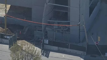 Vista aérea de una gran estructura de concreto parcialmente derrumbada, con escombros, barras de refuerzo expuestas y una cinta de seguridad naranja en el frente