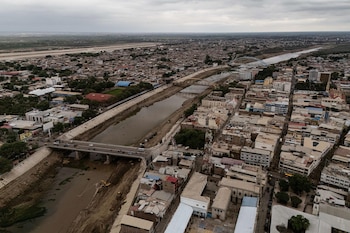 Fotografía aérea de una ciudad con un río canalizado atravesado por puentes vehiculares, edificaciones urbanas y cielo nublado