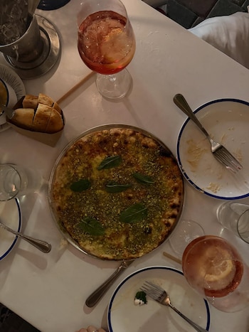 Vista aérea de una mesa de restaurante con un platillo principal con pistachos y menta, copas con cócteles rojizos, pan y platos semivacíos