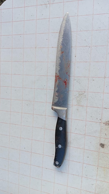 Un cuchillo de cocina con mango negro y hoja metálica manchada de sangre, apoyado sobre una superficie blanca cuadriculada