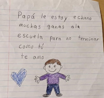 Primer plano de una nota en papel con renglones, texto manuscrito de un niño, un dibujo de un niño sonriente y un corazón azul