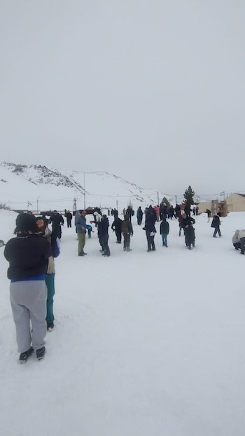 Vista frontal de un grupo de personas en un campo de nieve. Al fondo se aprecian montañas nevadas y un cielo nublado