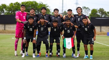 Diez jóvenes futbolistas de la selección de México posan en un campo de césped. Nueve usan uniforme oscuro, uno rosa. Un jugador sostiene un banderín mexicano.