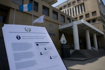 Un documento impreso sobre cuentas falsas se observa en primer plano frente al edificio del Ministerio Público de Guatemala.