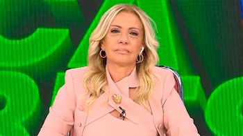 Susana Roccasalvo, una mujer rubia con cabello ondulado, viste un blazer rosa y aros, sentada frente a un fondo verde brillante