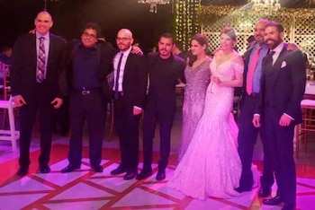 Grupo de siete personas, cinco hombres con traje y corbata, y dos mujeres con vestidos de fiesta, posando de pie en un espacio con iluminación y decoración