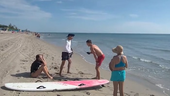 Una mujer sentada en la arena se toma la cabeza junto a una tabla de rescate mientras tres personas conversan de pie en la playa
