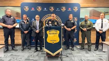 Siete hombres, incluyendo oficiales y un funcionario, de pie ante un podio con el logo de la Policía de Laredo. Al fondo, un banner azul y una pantalla con contenedores de carga