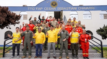Personas con uniformes militares, de rescate y chalecos amarillos posan con la mano levantada en las escaleras exteriores de un edificio blanco.