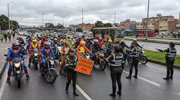 Agentes uniformados con un cartel de pare detienen a decenas de motociclistas con diversos disfraces en una avenida con autobuses urbanos al fondo.