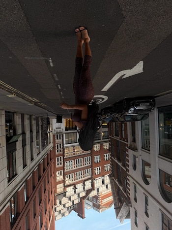 Fotografía vertical e invertida de una mujer de pie en una calle rodeada por edificios y un vehículo