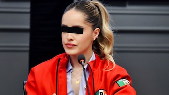 Una mujer con coleta y una franja negra sobre los ojos viste una chaqueta roja frente a un micrófono en una sala
