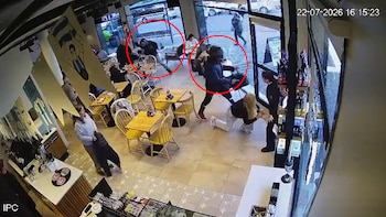 Vista aérea de un café con varias mesas y sillas. Un asaltante agrede a una mujer en el suelo mientras otro sujeta a un hombre en una mesa