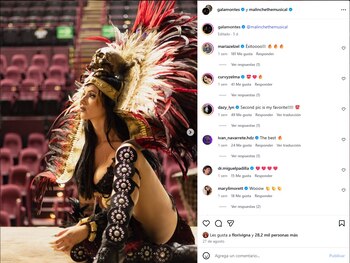Una mujer con penacho de plumas rojas y vestuario ceremonial posa sentada en un escenario frente a las butacas vacías de un teatro