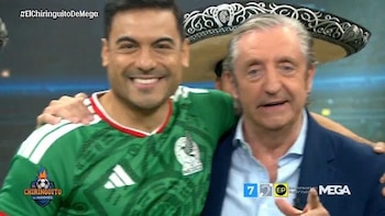 Dos hombres posan para una foto, uno con camiseta verde de México y otro con chaqueta azul, con un sombrero tradicional mexicano detrás
