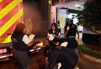 Cuatro personas con chalecos de la ONPE y un policía descargan cajas de un camión con franjas reflectantes rojas y amarillas por la noche, en un área exterior