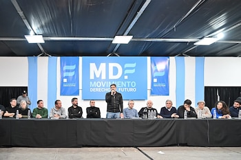 Andrés Larroque habla por micrófono. Detrás, doce personas sentadas en una mesa y un banner azul con 'MDF Movimiento Derecho al Futuro'