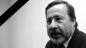 Hombre con barba y traje, mirando hacia la derecha. La imagen en blanco y negro incluye una cinta diagonal negra de luto en la esquina superior izquierda.