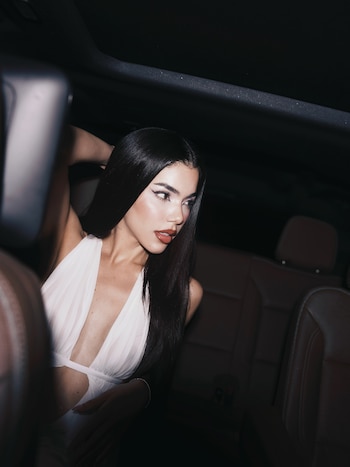 Mujer de cabello negro y largo con vestido blanco de escote profundo en el asiento de un automóvil